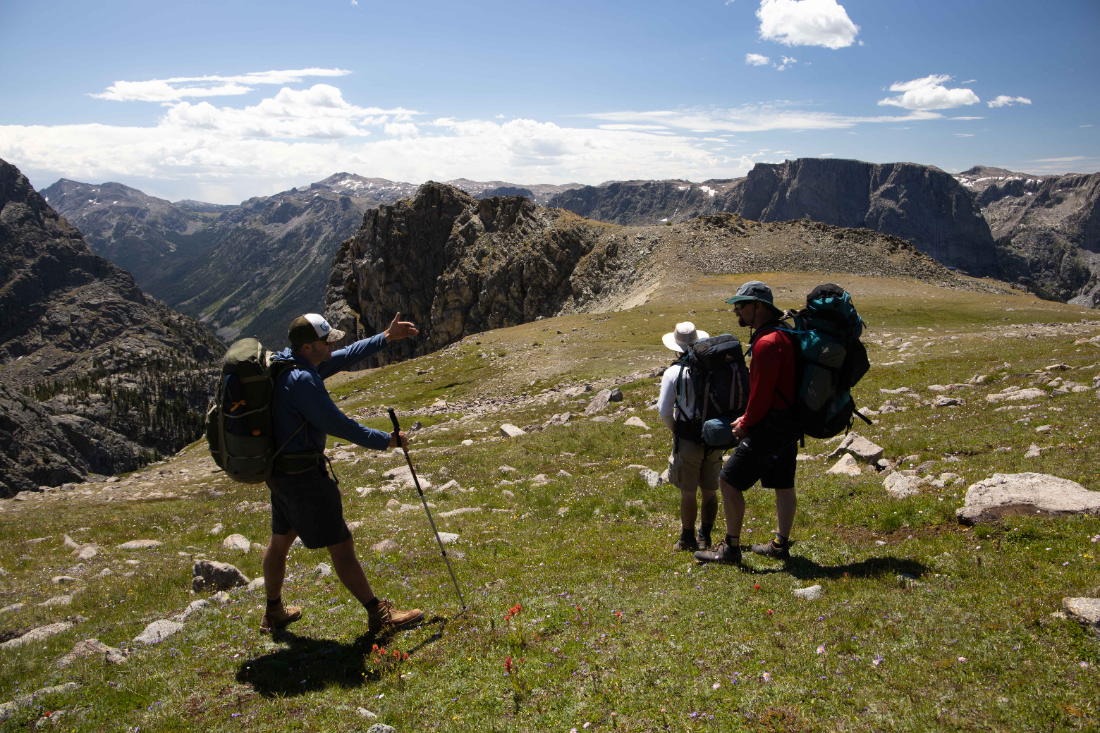 Three backpackers pausing on a high ridge to take in the view