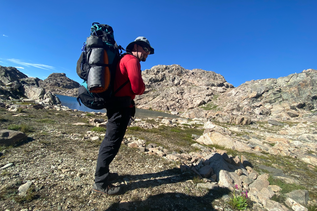A hiker descending granite slabs toward an alpine lake beneath towering Wind River peaks
