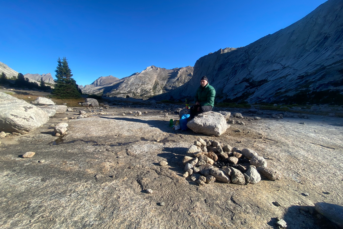 A climber resting at a backcountry camp beneath granite walls